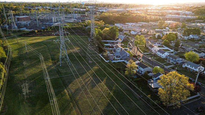 Power lines crossing a field next to a suburban neighborhood.