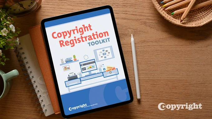 A table displays the words "Copyright Registration Toolkit" with a graphic of an infographic. The tablet sits on top of two notebooks which sits on top of a wooden desk. Surrounding the notebooks and tablet is a coffee cup, and pencils.  