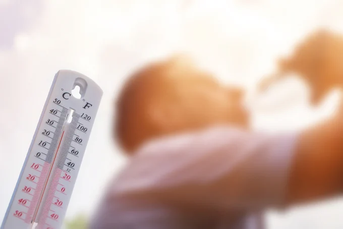 Thermometer showing a temperature around 30°C with a blurred person in the bright background.