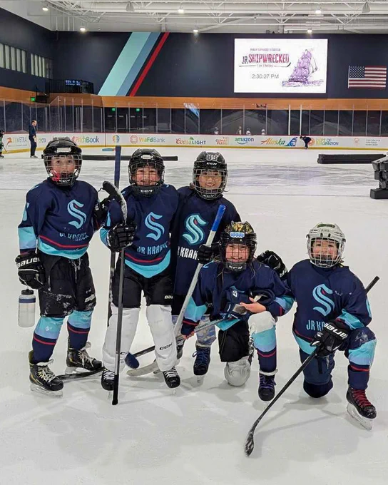 Youth hockey team photo on an indoor ice rink wearing navy Jr Kraken jerseys.