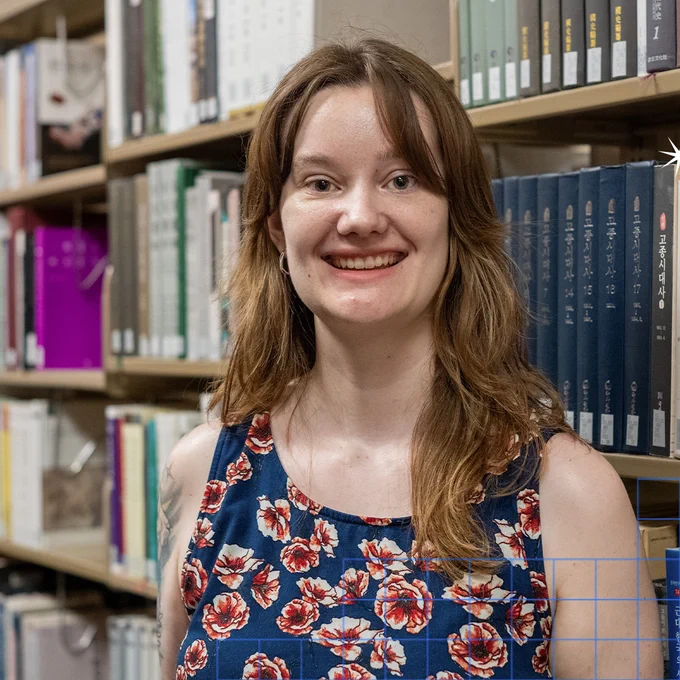 Daphne Tibbetts in front of a portion of the East Asian Collection in Watson Library.
