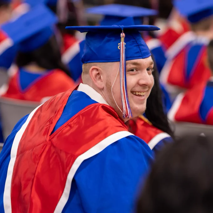 A smiling graduate in a blue cap and red gown at a graduation ceremony.