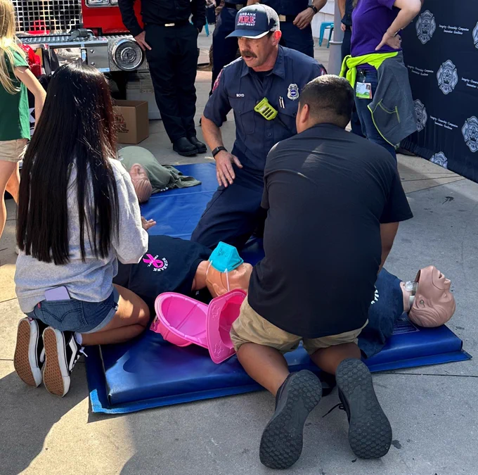 Two people learning how to do hands-only CPR from a Burbank firefighter