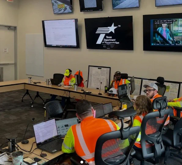Workers in high-visibility safety vests monitor multiple screens in a Texas Department of Transportation control room.