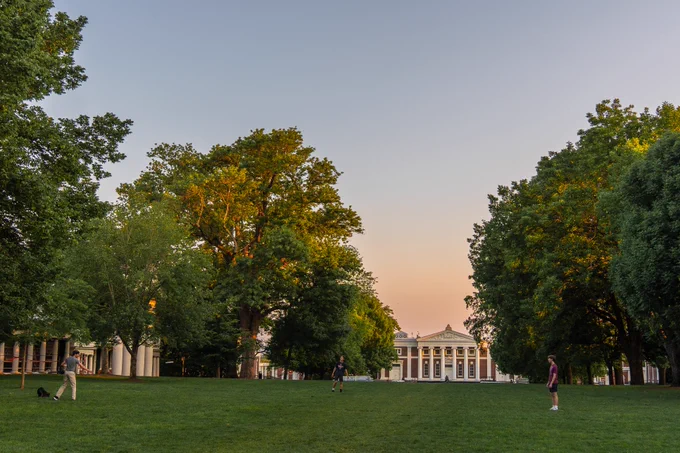 Three students on the Lawn at UVA surrounded by lush trees at sunset. In the background, Old Cabell Hall is visible. 