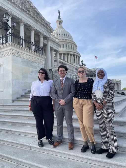 Four people stand on stone steps with the dome of the U.S. Capitol building in the background
