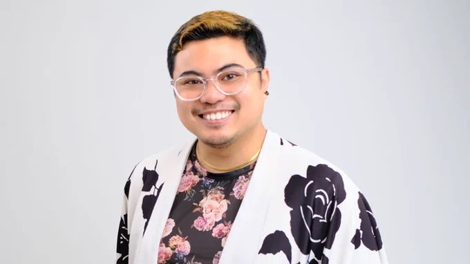 Angelico Obille smiles at the camera in a portrait against a light grey background. 