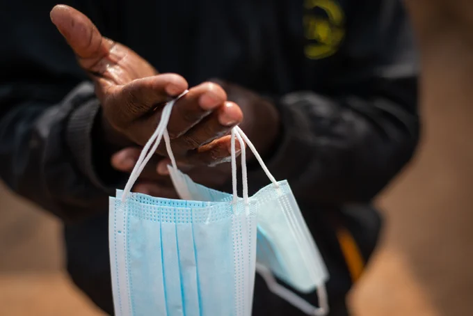 A person holding several disposable blue face masks in their hands. They are wearing a dark jacket, and the background is blurred.