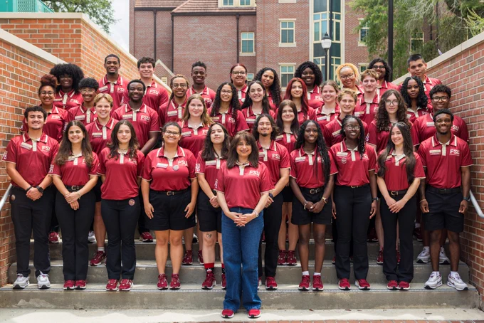 FSU First Lady Dr. Jai Vartikar stands with Orientation Leaders on stairs for a group photo. They are all smiling and wearing Orientation Leader polos.