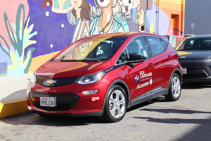 A red Chevrolet car parked on a city street with a vibrant mural in the background. 