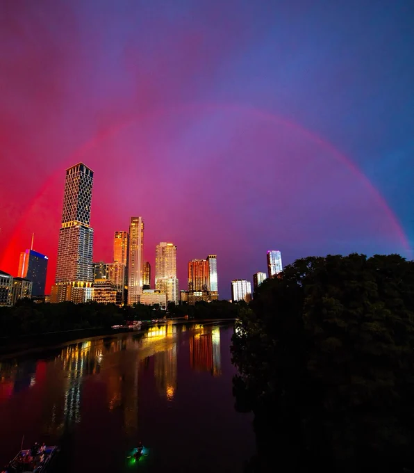 A rainbow arches across a bright purple, pink, and blue sunset over downtown Austin, TX.