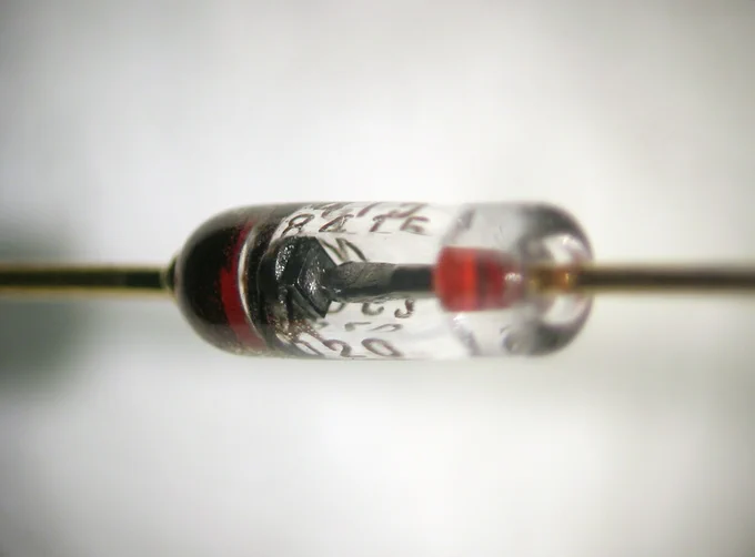 Close-up photo of a small black silicon diode with a visible black cathode band on the left side and exposed internal silicon between the leads.