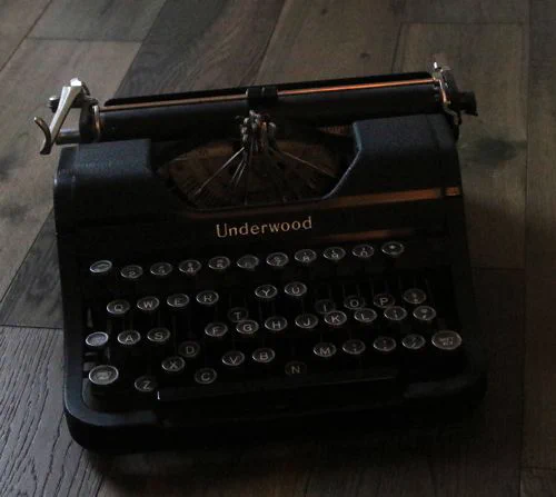 A closeup of a manual Underwood typewriter sitting on a wood plank surface.