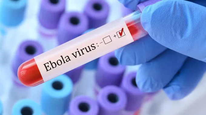 A gloved hand holds a test tube labeled "Ebola virus" with a positive check mark. The background shows several out-of-focus test tubes with purple caps.