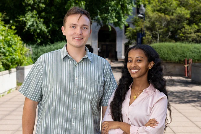 Emory undergraduates Andrew Conlon and Hlina Temesgen are standing outside on a pathway leading to the Quad lined with greenery and trees. 