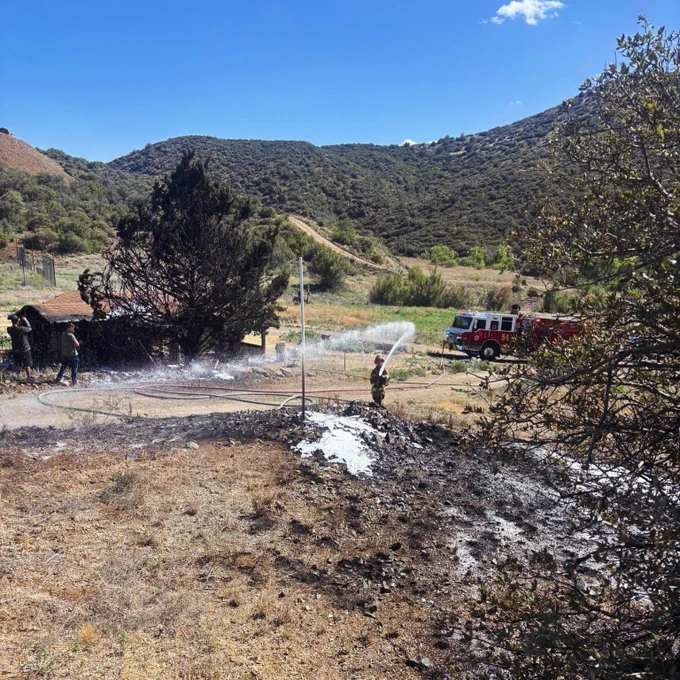A firefighter sprays water on the burnt grass of a wildland fire.