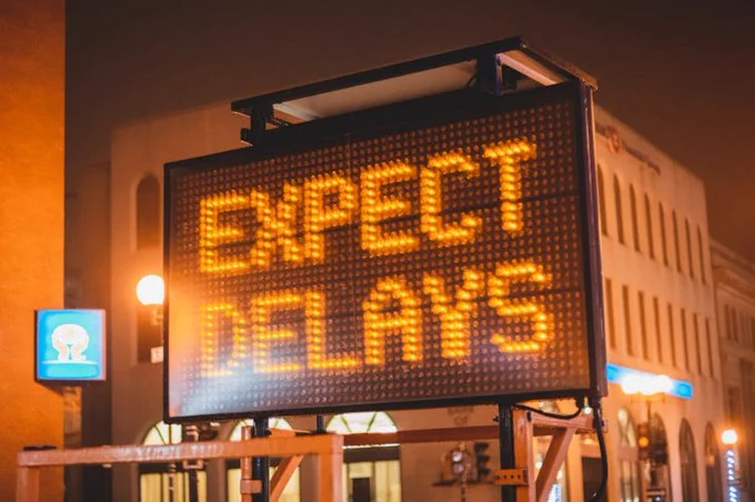Mobile electronic traffic sign with inscription Expect delays placed on road in city street in evening time
