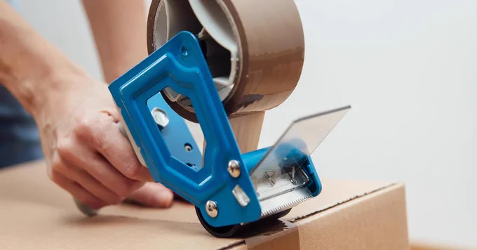 Person using tape dispenser to package cardboard box