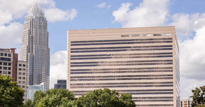 Charlotte cityscape featuring the Charlotte-Mecklenburg Government center and Bank of America tower against a sunny sky with white clouds.