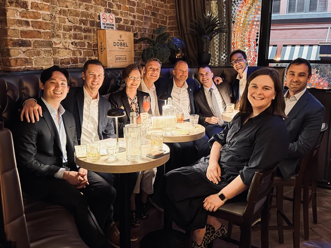 Nine people sitting around a bar table with an explosed brick background