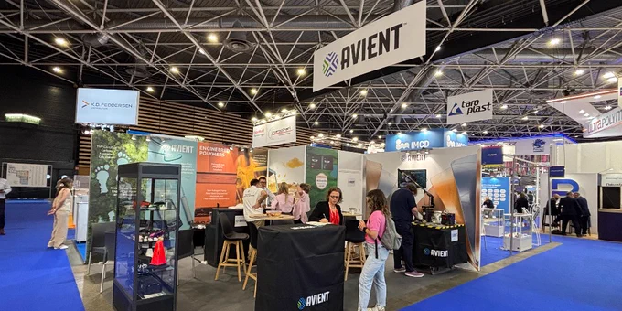 The image shows a bustling trade show booth for Avient, with banners and displays featuring product information. Attendees are interacting at the booth, which includes tables and promotional materials. 