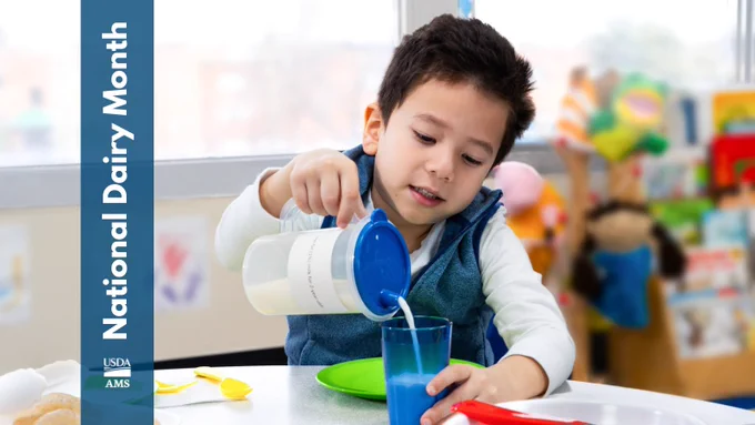 A person is pouring milk from a jug into a blue glass at a table with colorful utensils. The left side displays a vertical banner with the text "National Dairy Month" and logos of USDA and AMS.