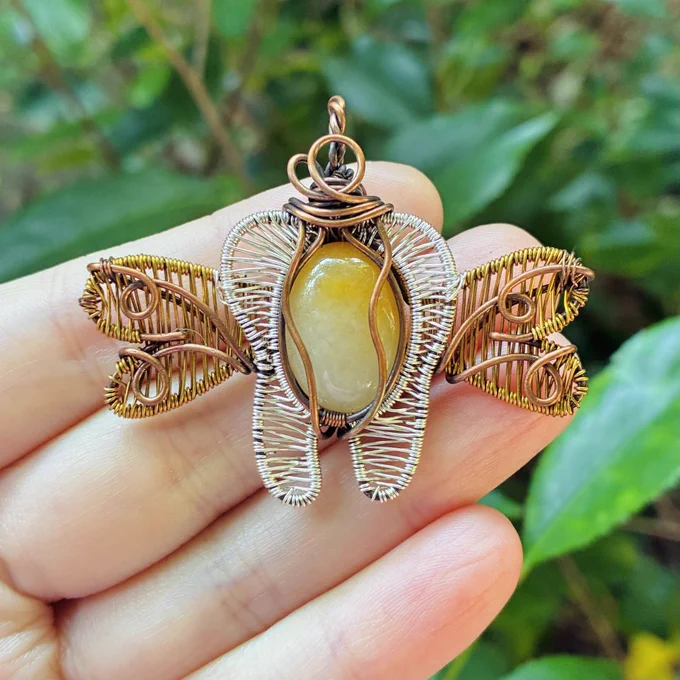 copper wirewrapped pendant in the shape of a tooth with wings with a white & yellow stone, silver weaved tooth, and gold weaved wings