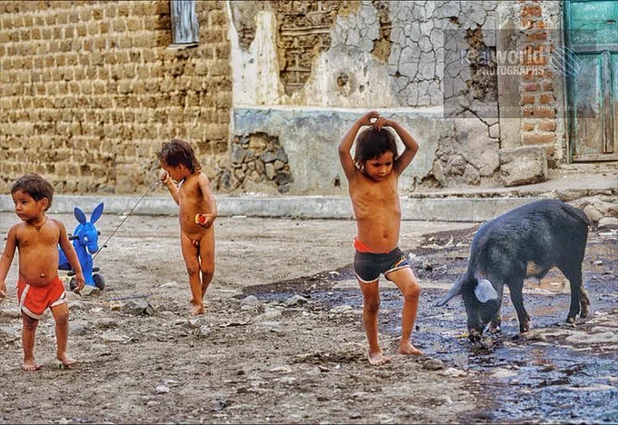 Children play next to a scavenging pig in San Gerardo, San Miguel, El Salvador, Central America. 1992. Gary Moore photo. Real World Photographs. #photojournalism #Nikon #ElSalvador #Grok #poverty #streetphotography  #realworldphotographs #travel #Copenhagen #garymoorephotography