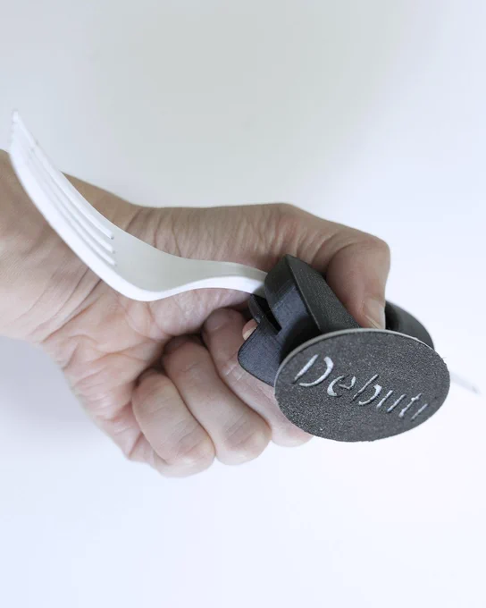 Mano sujetando un tenedor con engrosador negro impreso en 3D personalizado con la palabra “Debuti”.