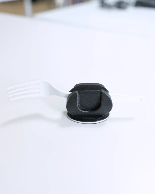 Engrosador negro impreso en 3D con un tenedor blanco, visto de perfil sobre fondo claro.