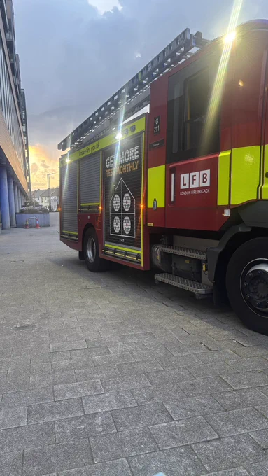 A fire truck parked outside of our building with a sunset backdrop, its ladder is displayed and part of trident point is visible.