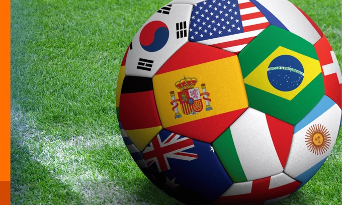 A football adorned with national flags, resting on a green football pitch.