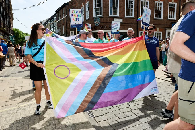 TransPennine Express colleagues at York Pride parade holding a Pride flag. A woman in a blue t-shirt smiles as she holds the flag.
