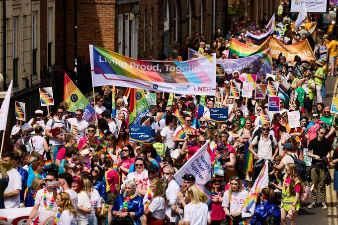 A Pride parade with rainbow flags and banners, featuring a large crowd celebrating together.