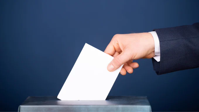 A hand puts a ballot paper into a ballot box. 
