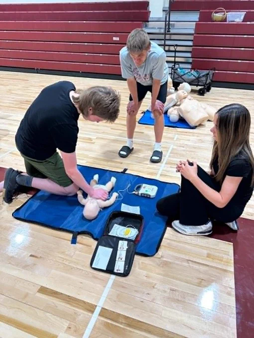 three students, one doing chest compressions, the other getting the AED ready and the other watching