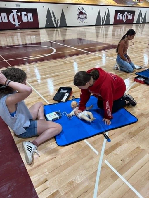 two females one performing chest compressions on a an infant mannequin