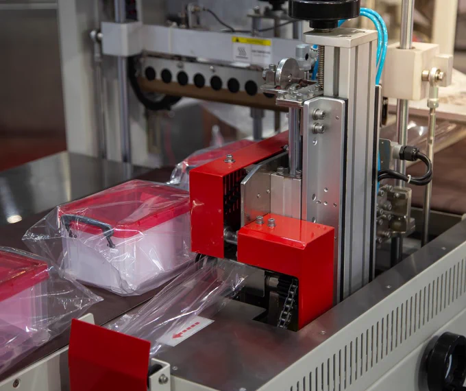 Small plastic containers on a conveyor belt being shrink wrapped.
