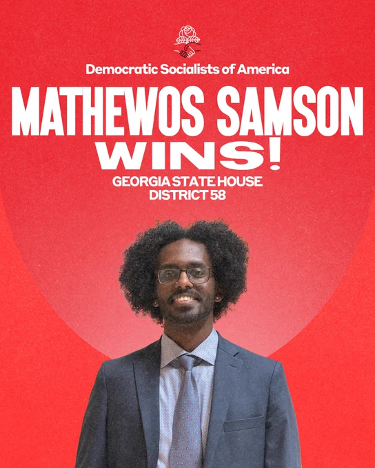 Mathewos Samson stands proudly wearing a navy blue suit and a shirt and tie which is a shade of periwinkle, and a big smile! 