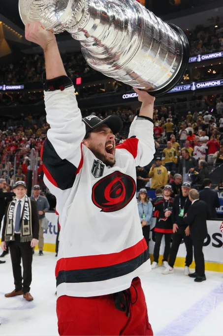 Photo of Sebastian Aho on ice lifting the Stanley Cup in a Hurricanes uniform.