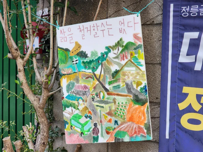 [삶을 철거할 수는 없다]
버스가 다니고 있는 정릉골의 알록달록한 정경 그림. 집 앞 나무에 걸려 있다.