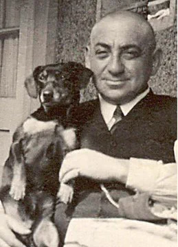 Elderly man seated outdoors with a small dog on their lap.
