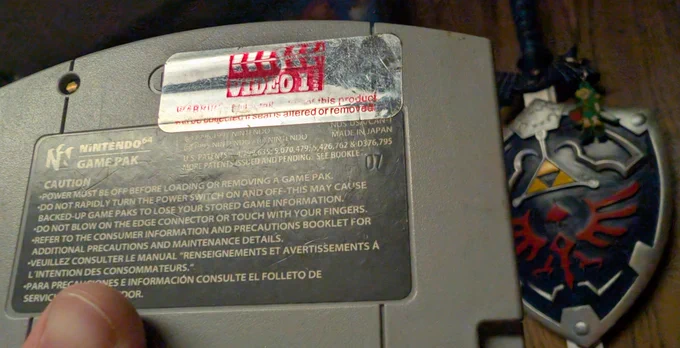 Two photos of a Nintendo 64 copy of The Legend of Zelda: Ocarina of Time. The front shows the gold label, while the back shows an old Video 1 rental sticker still attached. Back.
