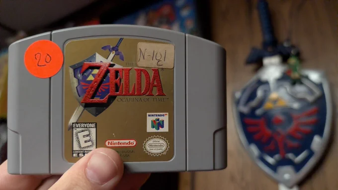 Two photos of a Nintendo 64 copy of The Legend of Zelda: Ocarina of Time. The front shows the gold label, while the back shows an old Video 1 rental sticker still attached. Front.