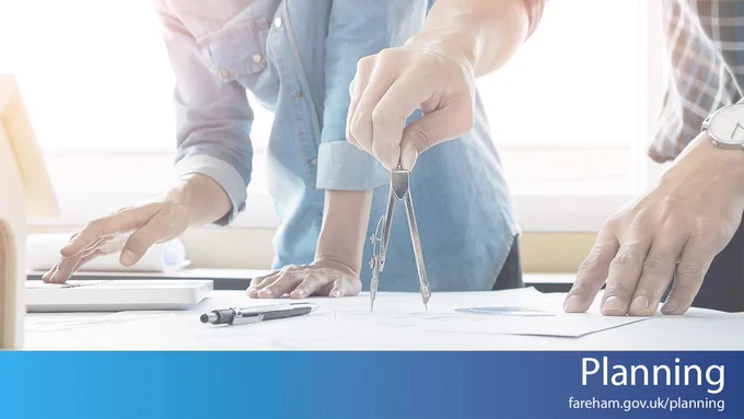 Photo of two people at a desk with paperwork and pen, with only their arms and hands visible; one person is using a compass and protractor. There is a blue bar at the bottom with the text "Planning fareham.gov.uk/planning"