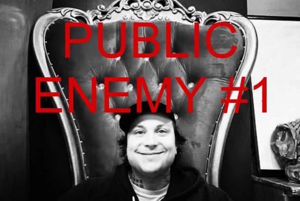 A black and white photo of Frank Iero smiling, the words "PUBLIC ENEMY #1" in red font above his head.