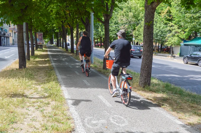 People of all ages and abilities walk, cycle, drive, and ride public transportation along the low-traffic streets of Bologna, which are lined with buildings, trees, bike infrastructure, and prominent 30 km/h speed limit signage and road markings.
