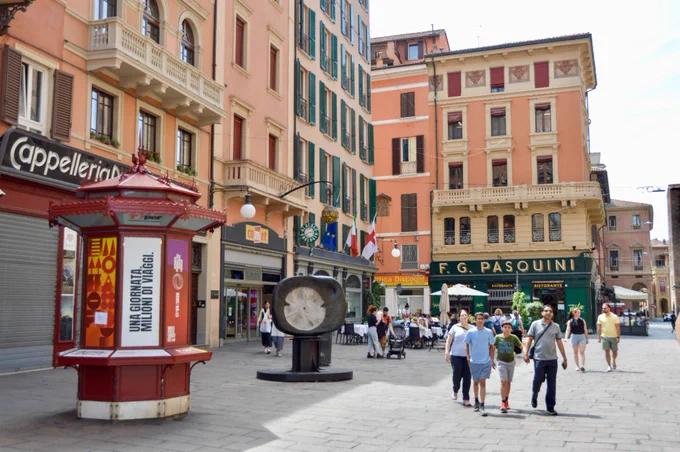 People of all ages and abilities walk, cycle, drive, and ride public transportation along the low-traffic streets of Bologna, which are lined with buildings, trees, bike infrastructure, and prominent 30 km/h speed limit signage and road markings.
