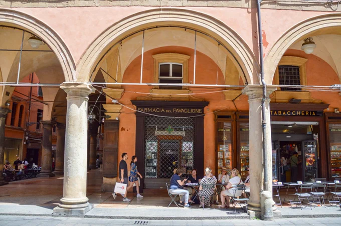 People of all ages and abilities walk, cycle, drive, and ride public transportation along the low-traffic streets of Bologna, which are lined with buildings, trees, bike infrastructure, and prominent 30 km/h speed limit signage and road markings.