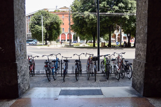 People of all ages and abilities walk, cycle, drive, and ride public transportation along the low-traffic streets of Bologna, which are lined with buildings, trees, bike infrastructure, and prominent 30 km/h speed limit signage and road markings.